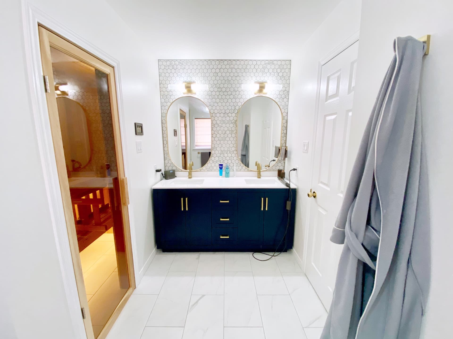 Primary bathroom with navy double vanity, metal fixtures and a sauna beside it